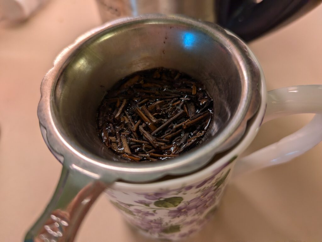 Kukicha tea stems (twigs) steeping in a strainer on top of a mug.